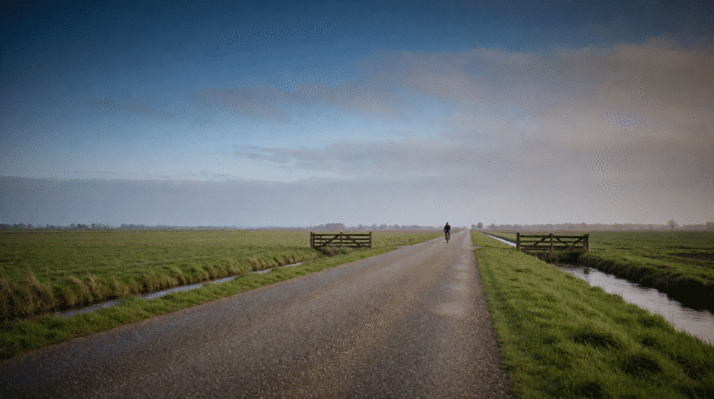 Long straight country road with a distant cyclist between green fields