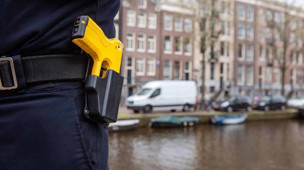 Yellow police taser in a holster on an officer's belt, with an Amsterdam canal in the background