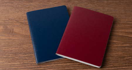 Two closed passports on a wooden desk next to a pen and a folder