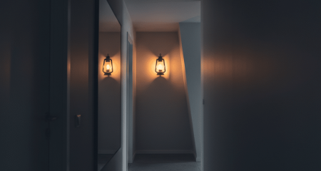 A dimly lit hallway with a flickering gas lamp casting distorted shadows, symbolising gaslighting as a form of psychological domestic violence.