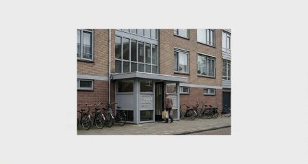 A mid-market Dutch apartment block on a quiet street with bicycles at the entrance