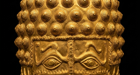 A professional archaeological studio photograph of the golden Dacian helmet of Coțofenești against a black background. The 4th-century BC beaten gold helmet features a striking face mask with two large, stylized eye motifs and a central nose guard. The dome is covered in a pattern of small, pointed conical studs, while the sides are intricately embossed with animal figures and spirals. The artifact rests on a minimalist dark display stand under warm, cinematic lighting that highlights the texture of the gold.
